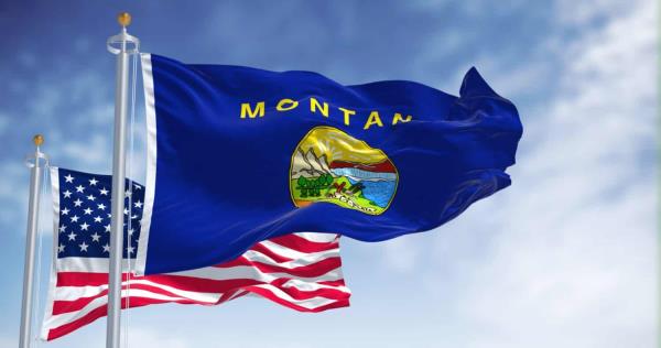 The Mo<em></em>ntana state flag waving along with the natio<em></em>nal flag of the United States of America. In the background there is a clear sky. Mo<em></em>ntana is a state in the western United States